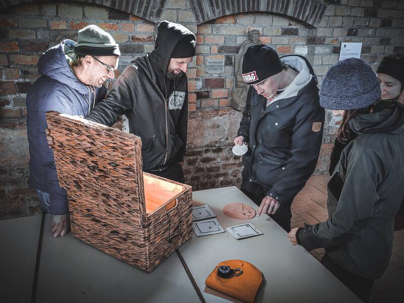 Fünf Personen stehen mit einem Rätsel aus der Truhe im Keller und tauschen sich über die Lösung aus.