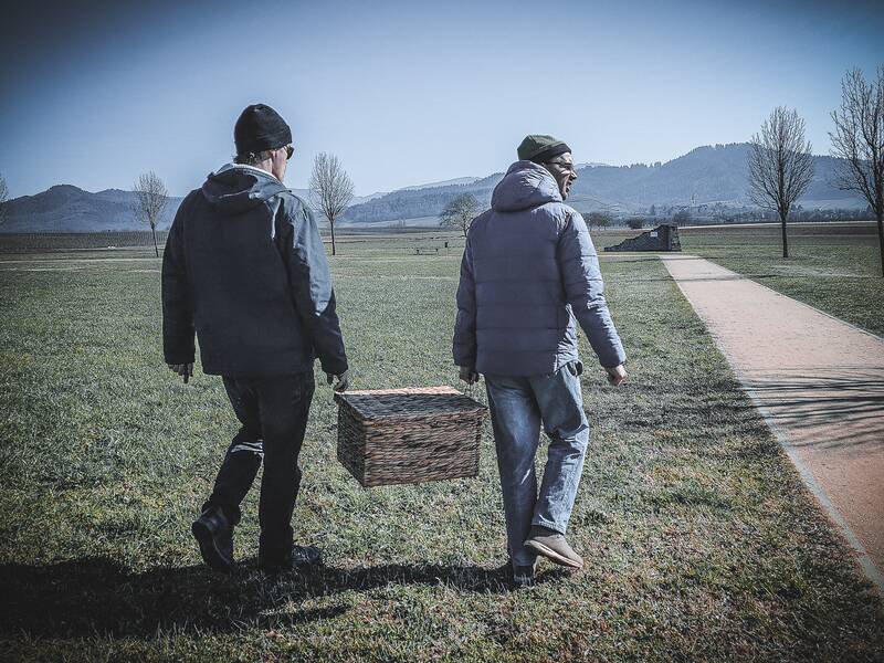 Zwei Männer tragen die Rätseltruhe gemeinsam durch den Römerpark.