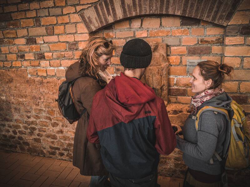 Drei Personen stehen im römischen Keller und unterhalten sich angeregt über eine Rätselfrage.
