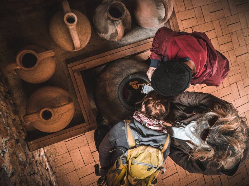 Blick von oben in den Keller, wo drei Personen in eine römische Amphore spähen.