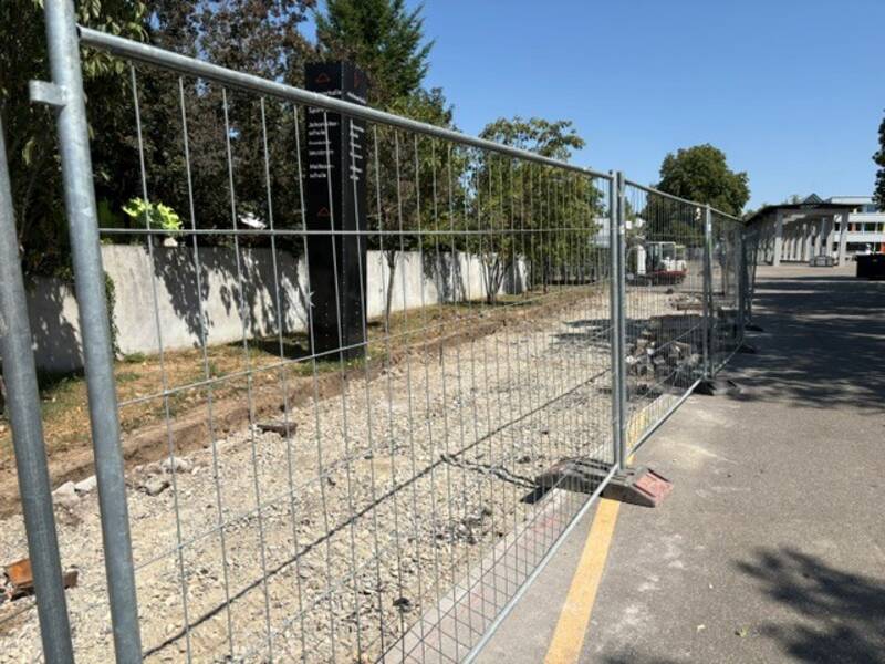 Hinter dem Bauzaun sieht man die aufgebrochene Asphaltfläche des Schulhofes, die begrünt wird.