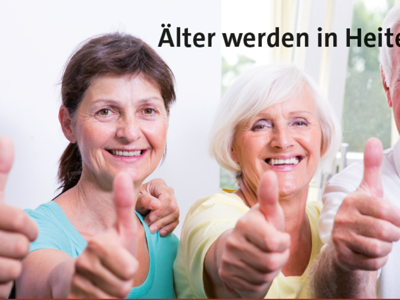 Eine Gruppe älterer Menschen lächelt und zeigt den Daumen hoch vor dem Text "Älter werden in Heitersheim".